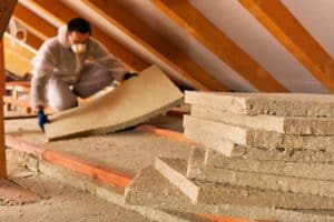 Worker installing fiberglass insulation between attic ceiling joists to improve home insulation and energy efficiency.