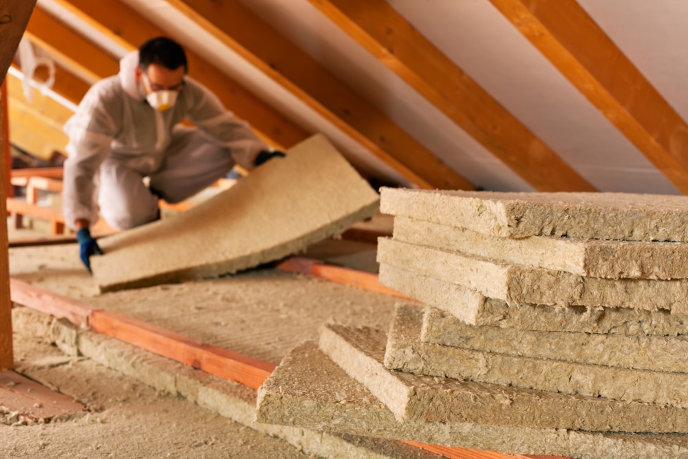 Worker installing fiberglass insulation between attic ceiling joists to improve home insulation and energy efficiency.